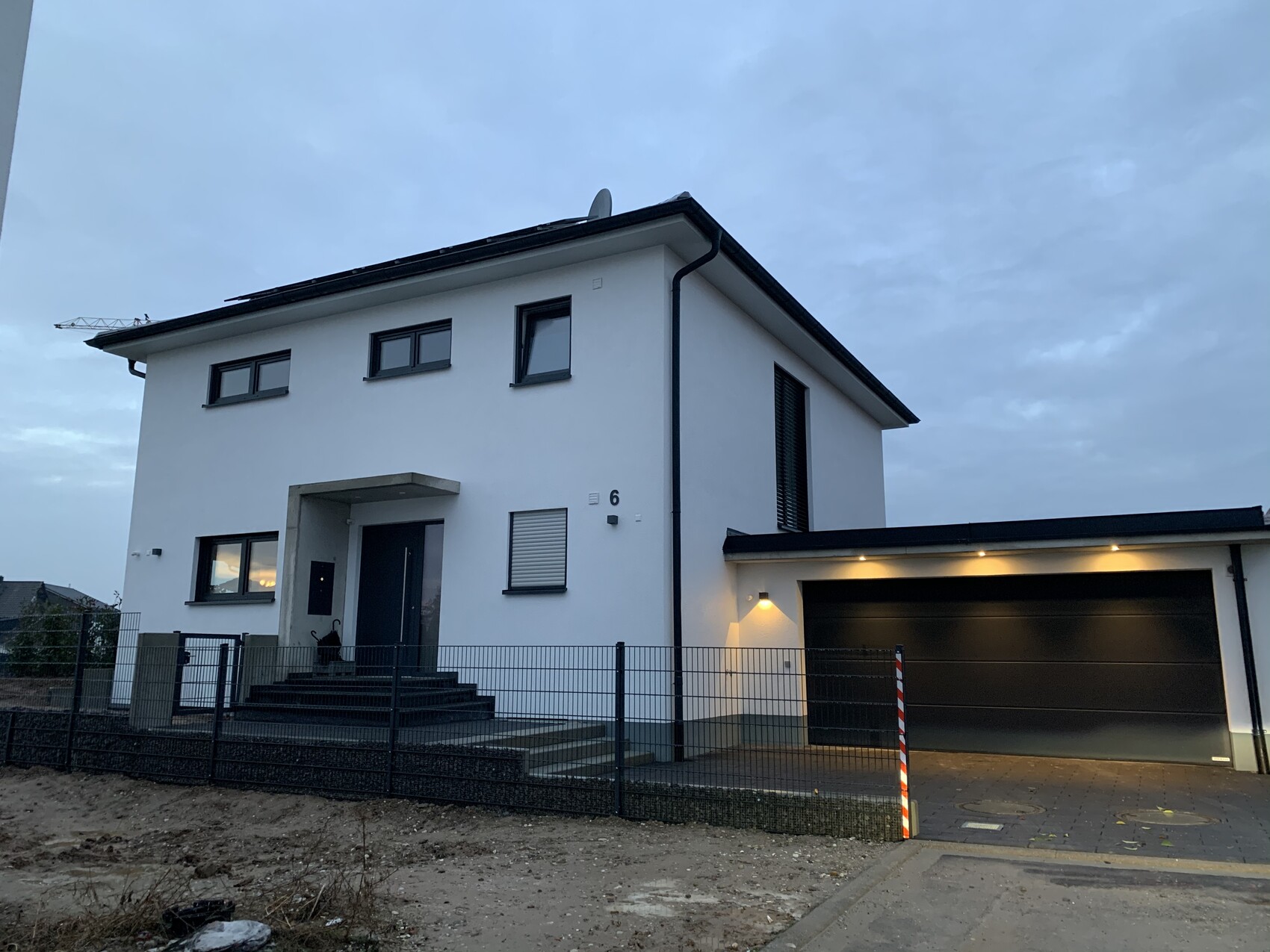 Modernes weißes zweigeschossiges Haus mit dunkler Garage, Treppe zum Eingang, Zaun davor.
