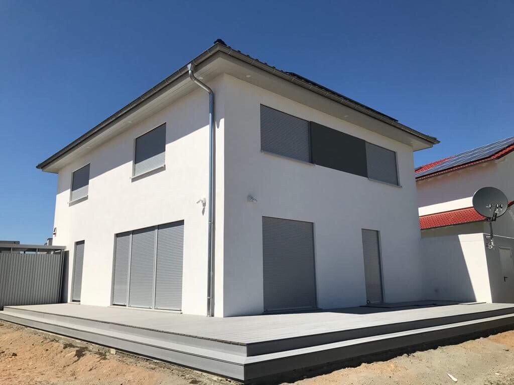 Weiße zweistöckige Hausfront mit großen Rollläden, Terrasse und Satellitenschüssel.