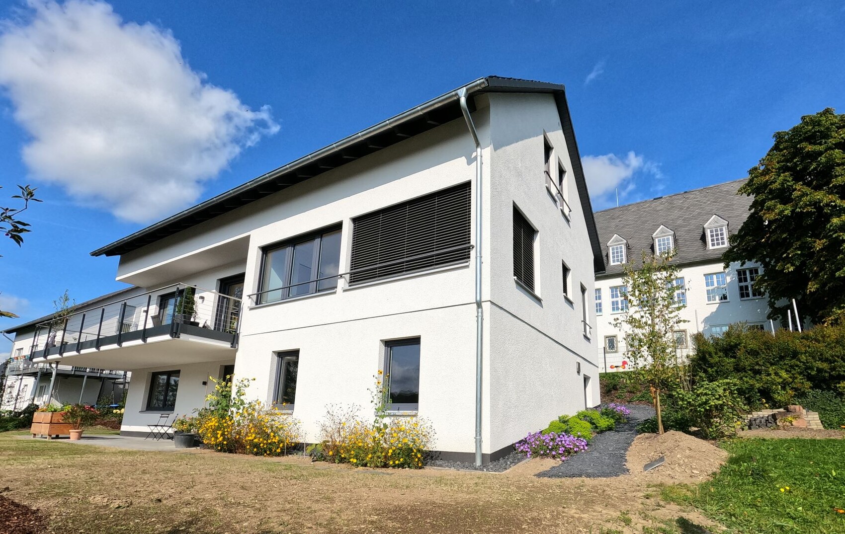 Außenansicht eines modernen weißen Wohnhauses mit Balkonen und Garten