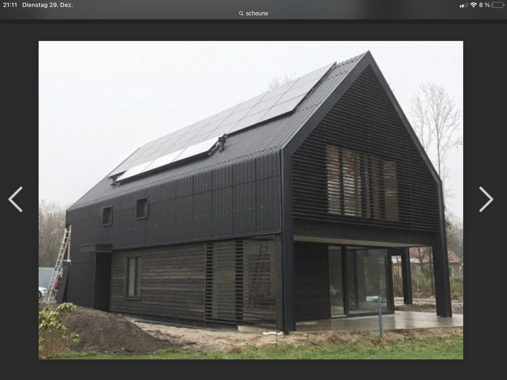 Modernes schwarzes Haus mit steilem Giebel, Solaranlagen auf dem Dach und Glasfront