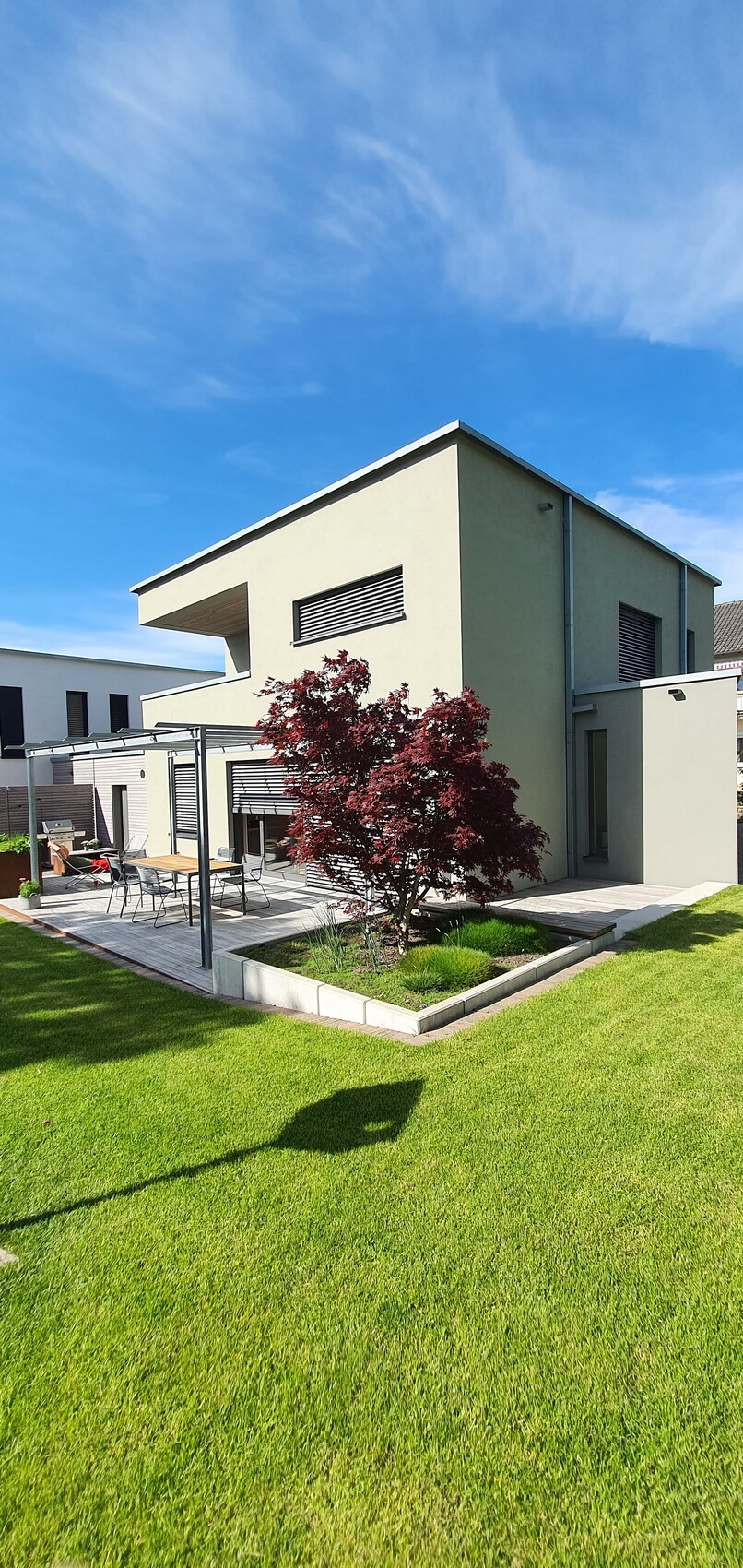 Modernes Einfamilienhaus mit Terrasse, grünem Rasen und rotem Ahornbaum vor blauem Himmel