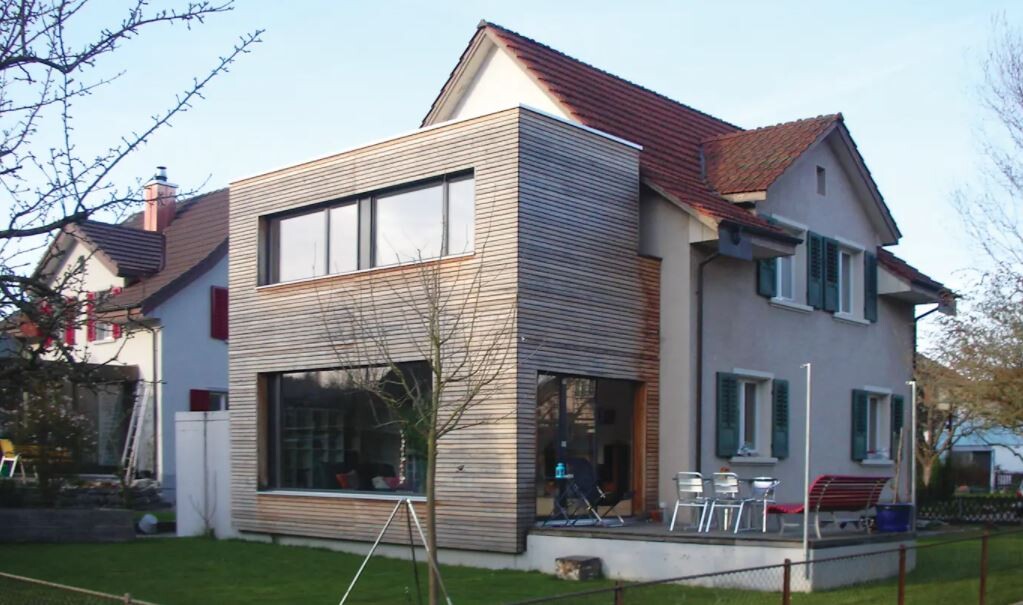Modernes zweigeschossiges Haus mit Holzverkleidung, Terrasse und Garten.