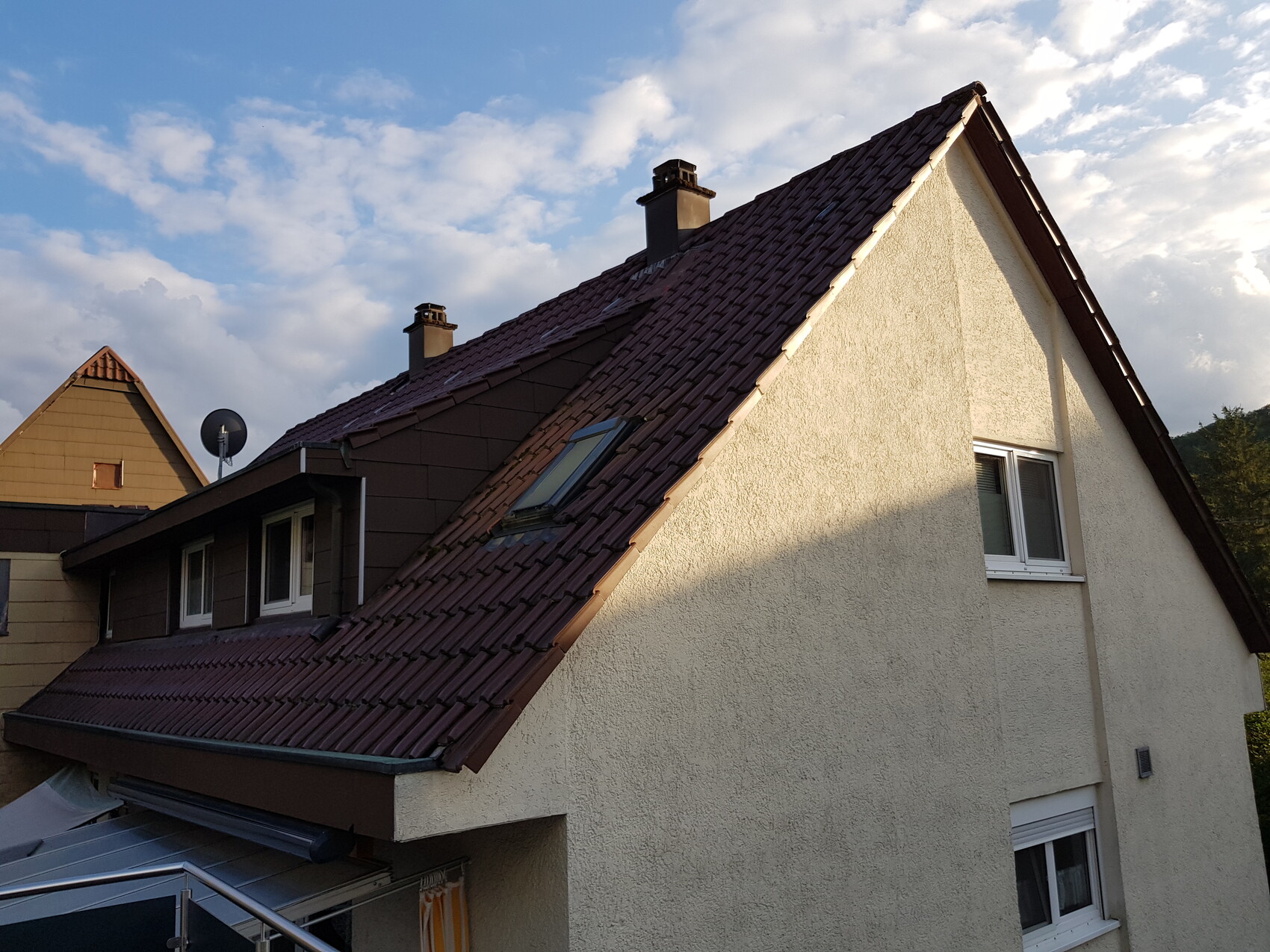 Dach eines Hauses mit rotem Ziegeldach, Dachfenster, weiße Fassade und Himmel im Hintergrund.