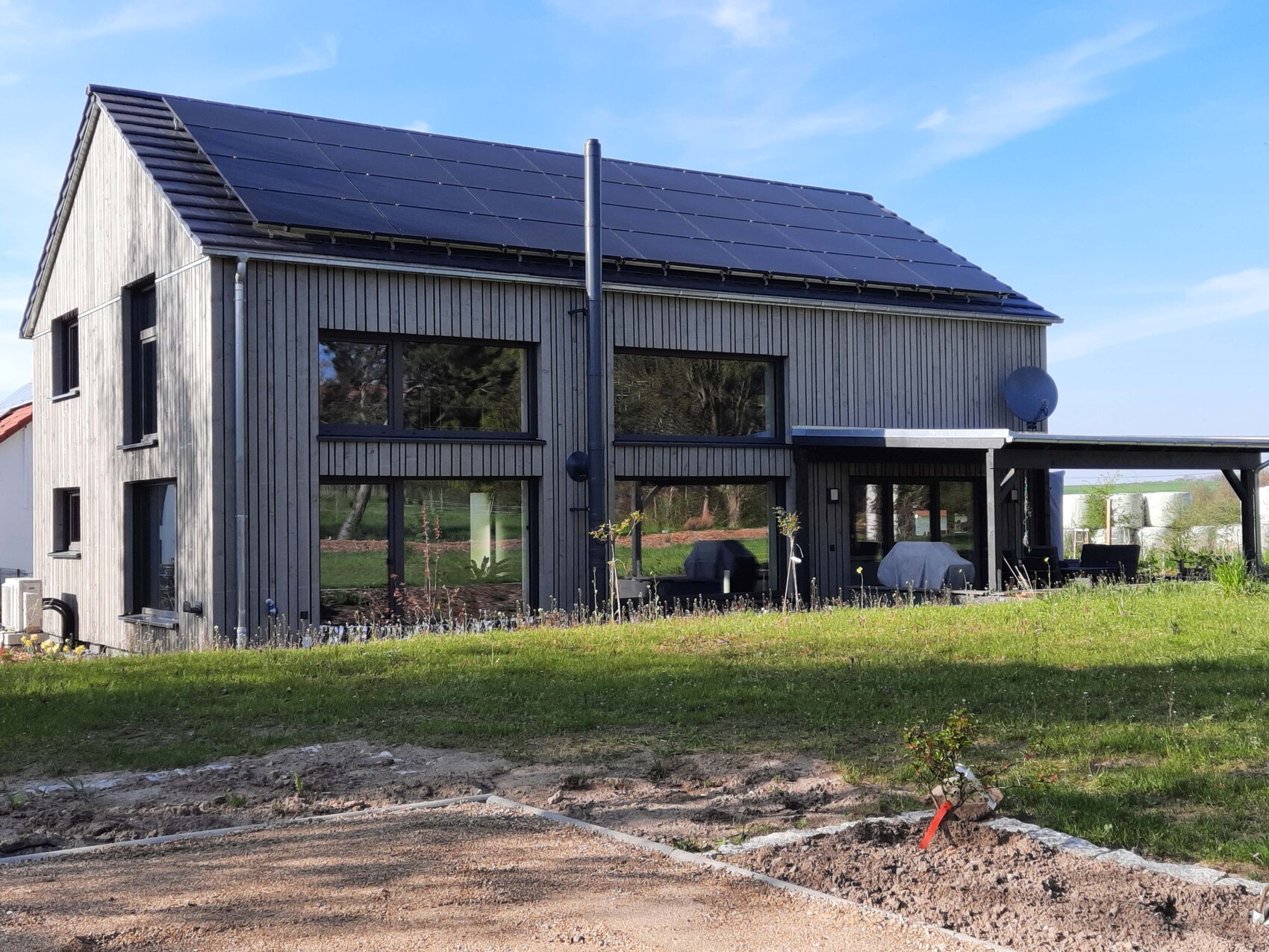 Modernes dunkles Holzhaus mit Solarpanels, großen Fenstern und Terrasse.