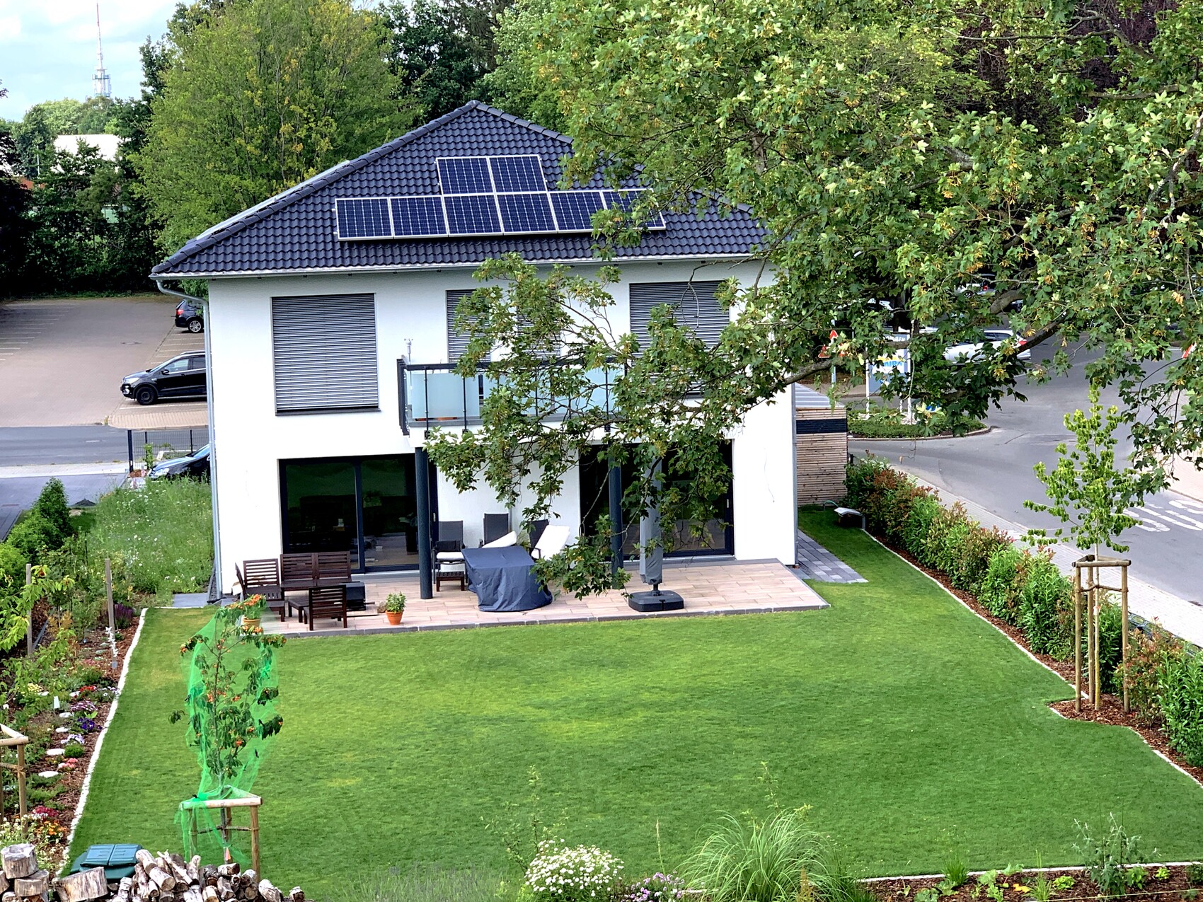 Modernes zweistöckiges Haus mit Solarpanelen auf dem Dach, Terrasse und gepflegtem Garten.