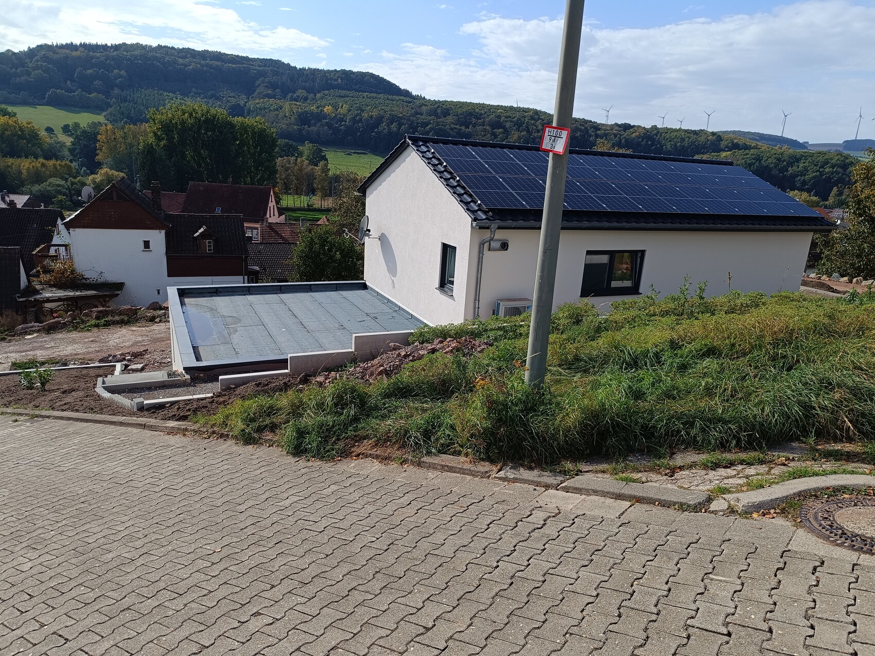 Weißes Einfamilienhaus auf Hang mit Solarpanelen auf dem Dach, grüne Umgebung.
