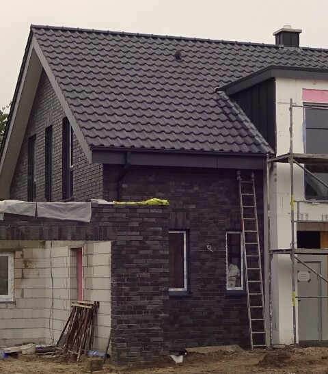 Unter Bau befindliches zweistöckiges Haus mit dunkler Backsteinfassade, Gerüst und Leiter.