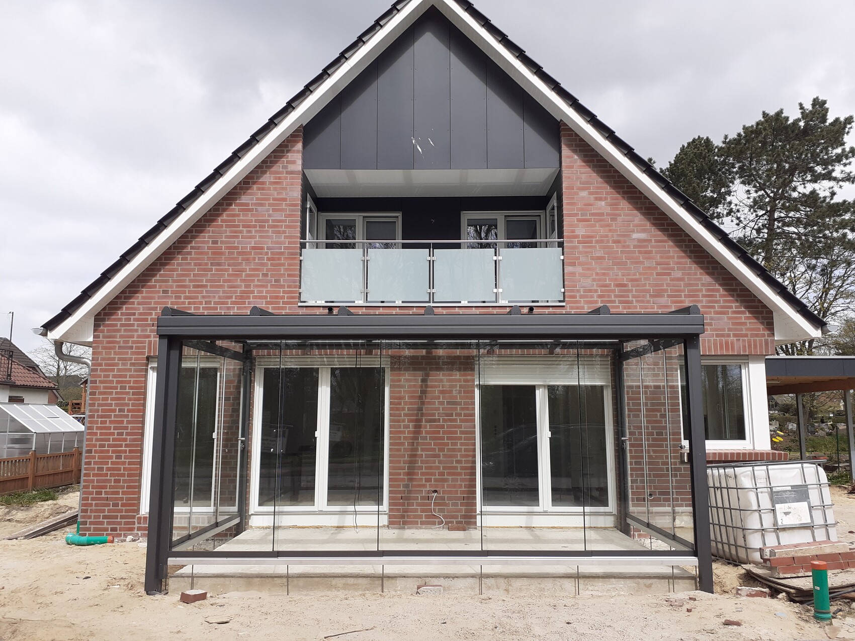 Modernes zweistöckiges Backsteinhaus mit Glas-Wintergarten und Balkon unter dem Dachfirst.