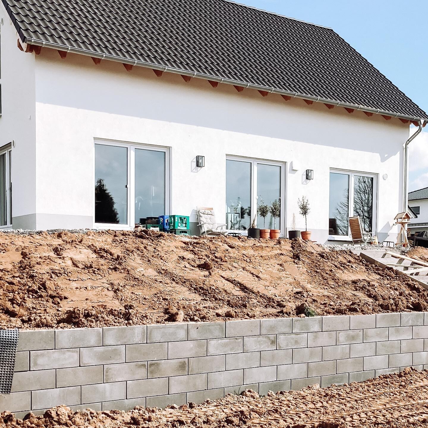Weißes Einfamilienhaus mit großen Glasfenstern, Erddamm und Betonmauer im Garten.