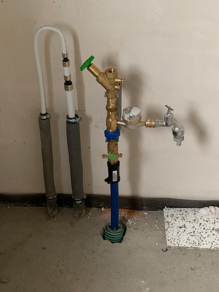 Wasserinstallations-Setup mit Zähler, Ventil, Armaturen und Rohren an der Wand.
