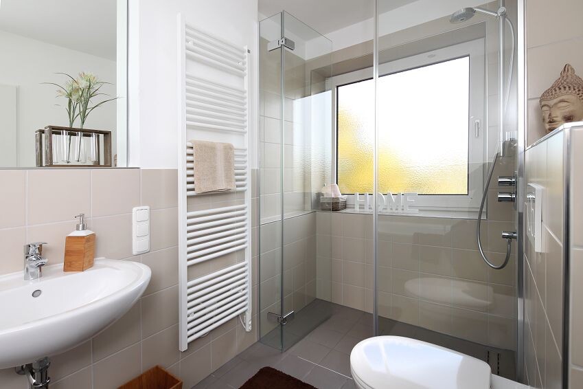 Modernes Badezimmer mit Glasdusche, Waschbecken, Handtuchheizkörper, Fenster und Buddha-Dekor.