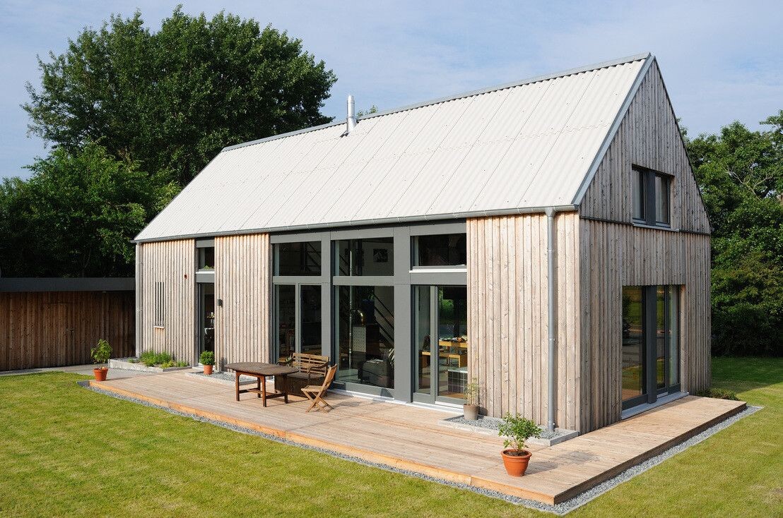 Modernes Holzhaus mit großer Glasfront, Holzterrasse und Garten.