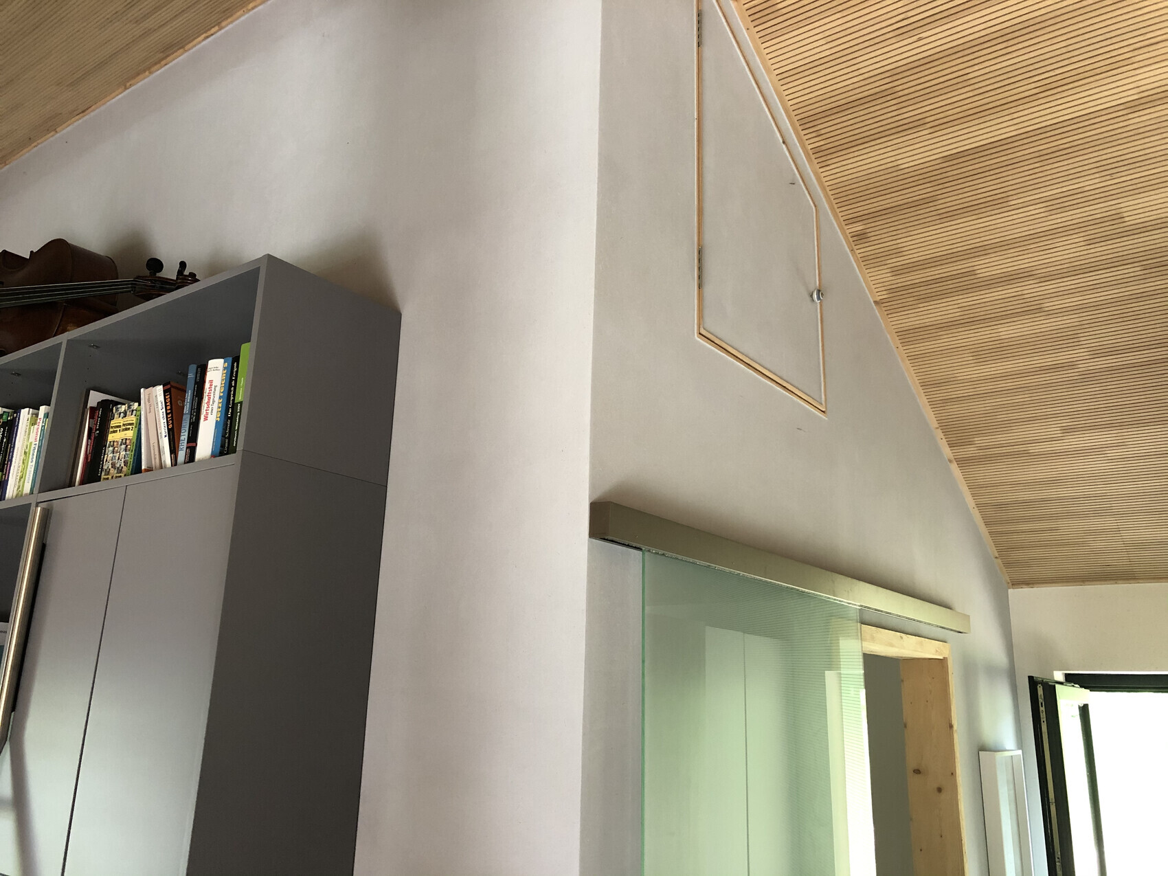 Moderner Innenraum: grauer Schrank mit Bücherregal, Geige liegt darauf, Holzdecke und Glas-Schiebetür.