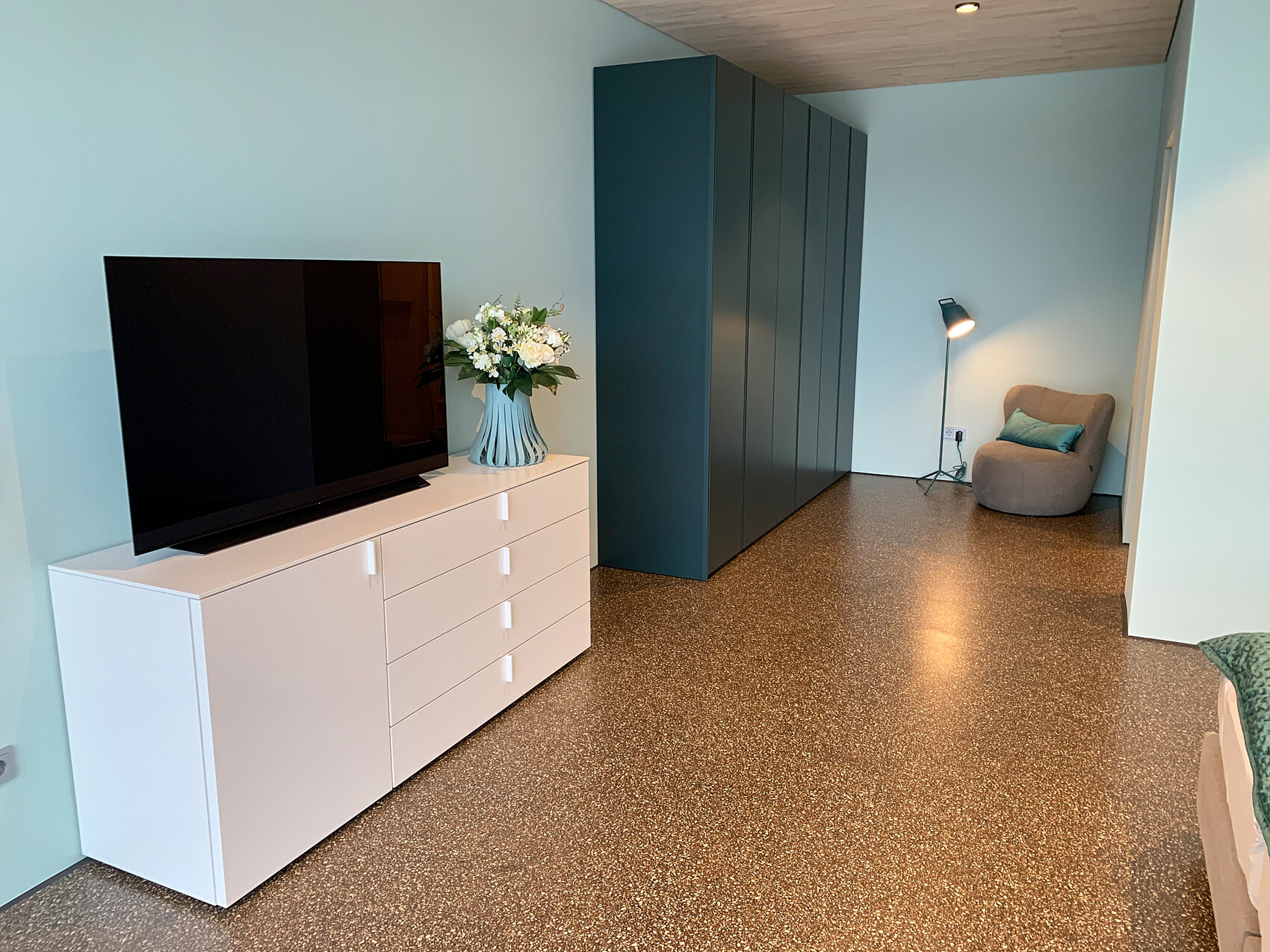 Modernes Wohnzimmer: TV auf weißer Kommode, Vase mit Blumen, blaue Wände, Schränke, Leselampe.