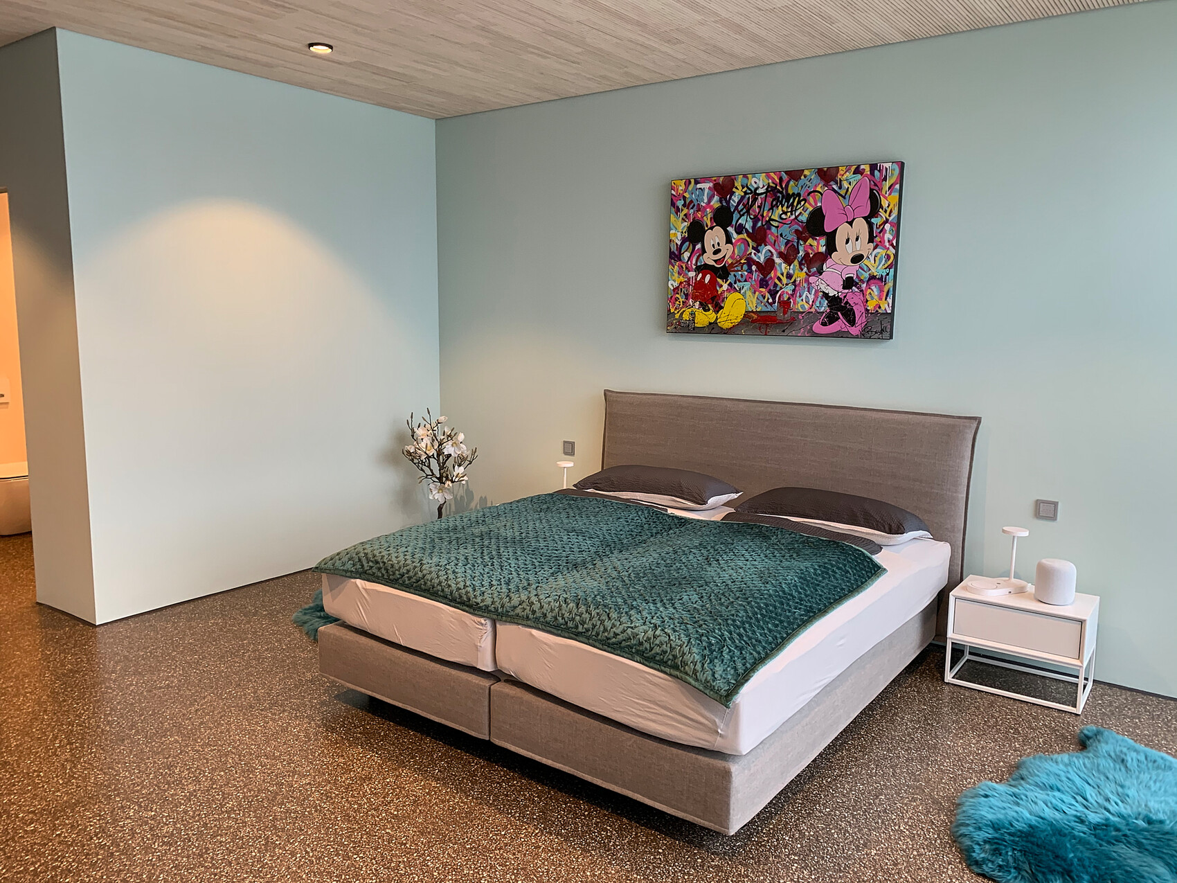 Schlafzimmer mit mintfarbenen Wänden, Bett mit grauem Kopfteil, Minnie/Mickey-Gemälde.