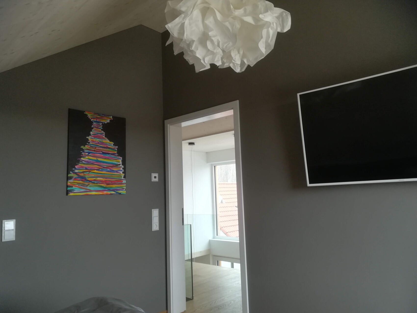 Wohnzimmer mit dunklen Wänden, buntes Baum-Gemälde, großer TV an Wand, Tür zum hellen Flur.