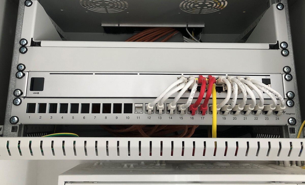 Patchpanel im Serverrack mit vielen weißen Kabeln, rote und gelbe Kabel, Ports 1–24 sichtbar.