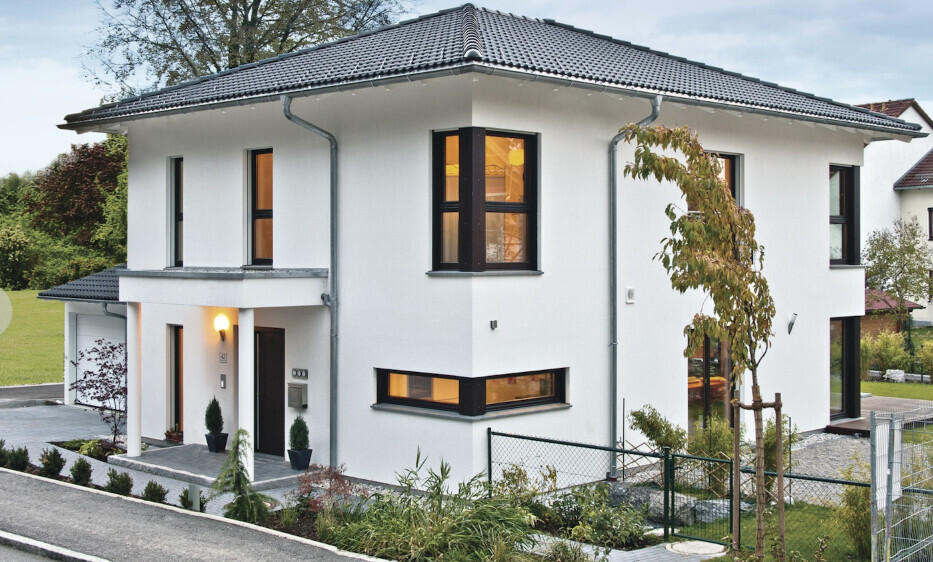 Modernes weißes Einfamilienhaus mit schwarzen Fensterrahmen, Garten und Zufahrt.