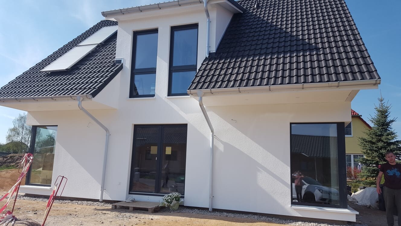 Modernes weißes Einfamilienhaus im Bau mit großen Fenstern und Ziegeldach.
