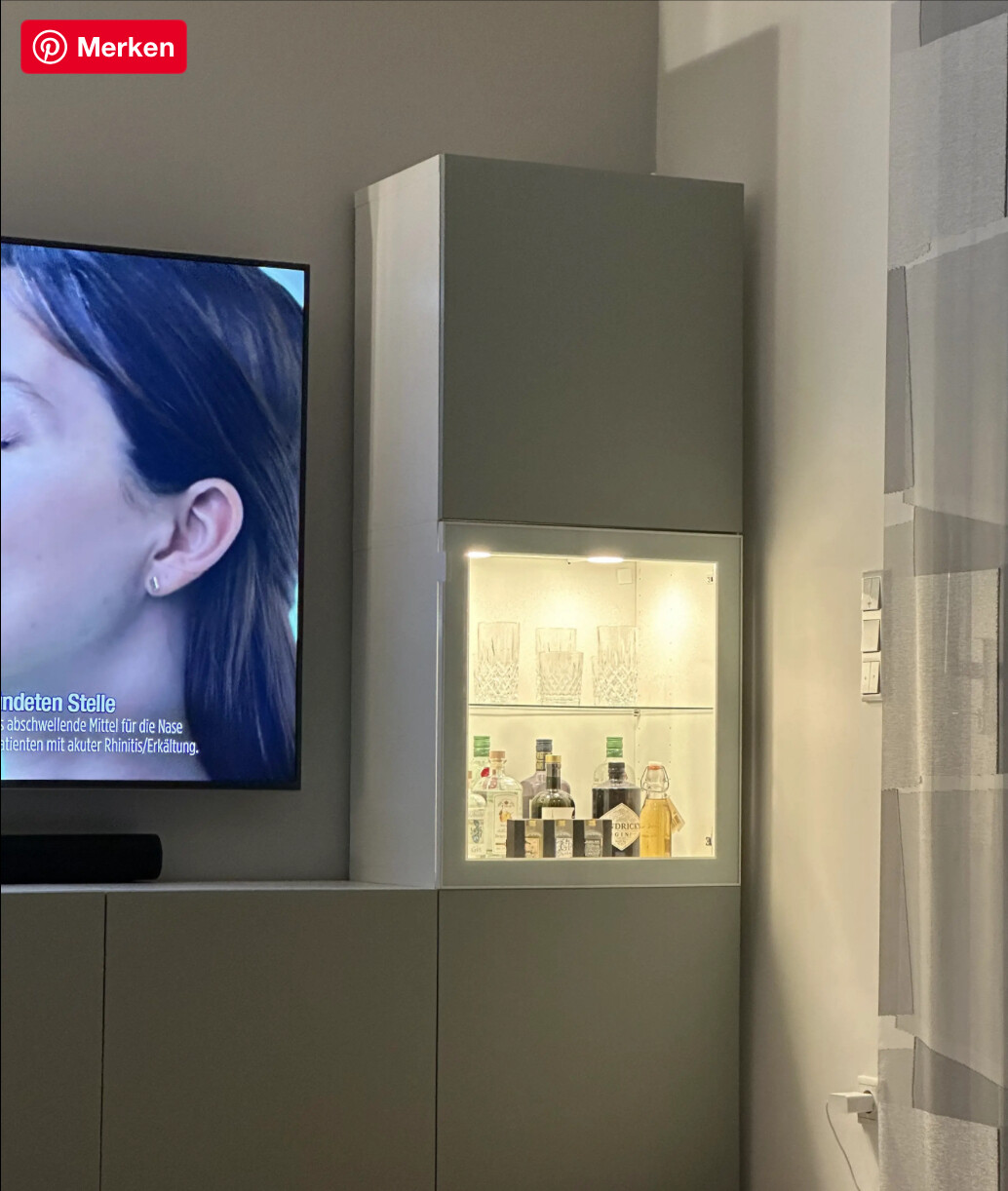 Moderner Wohnraum mit grauem Schrank, Glasvitrine mit Flaschen und Fernseher.