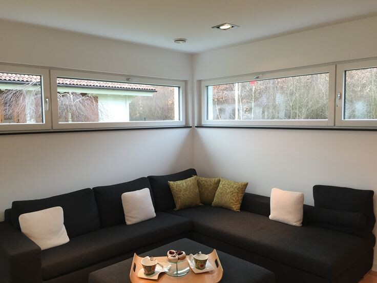 Helles Wohnzimmer mit dunkler L-förmiger Eckcouch, Fensterfront und Kaffeetisch