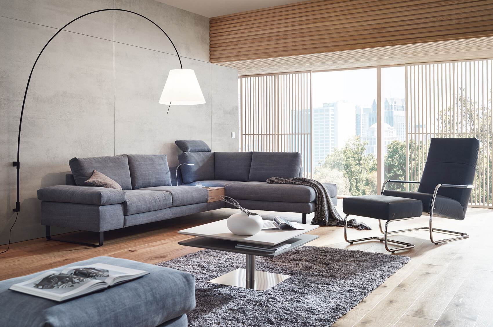 Moderne Lounge mit grauen Sofas, Sessel, Couchtisch und Stadtblick durch große Fenster.