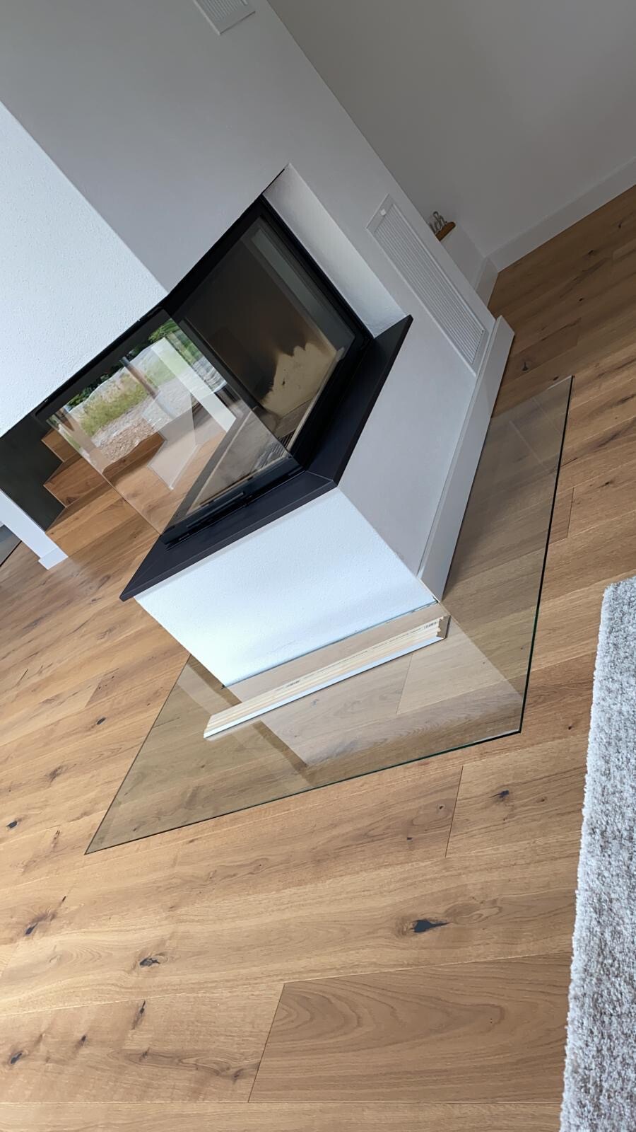 Moderner Kamin mit schwarzer Glasfront in weißem Raum, Holzfußboden, Glas-Tisch davor.