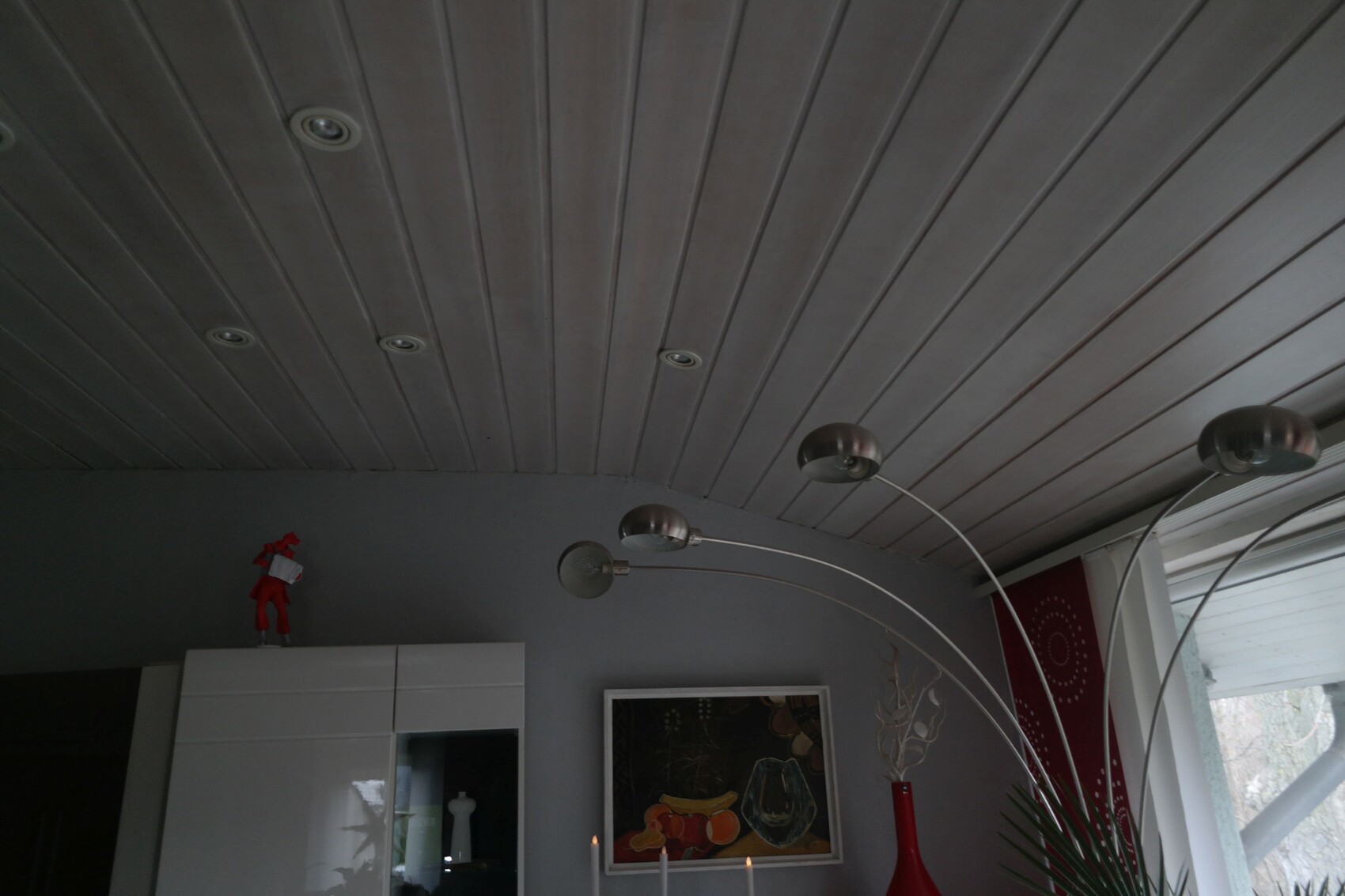 Modernes Wohnzimmer mit Bogenlampe, grauer Wand, weißem Schrank, roter Figur oben, Gemälde.