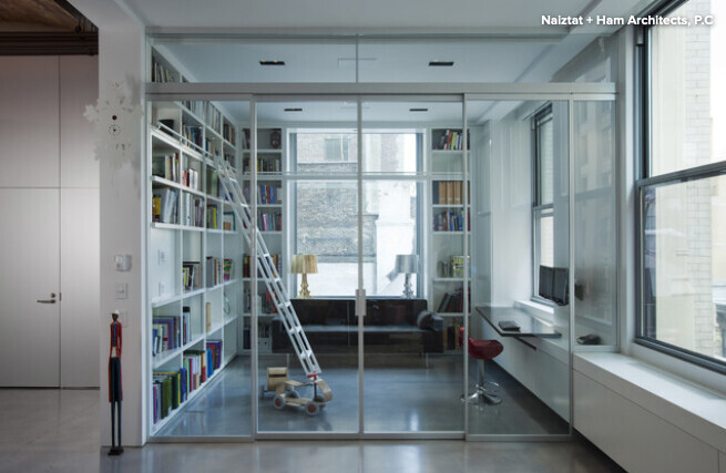 Offenes Wohnzimmer mit Glastrennwand, links Bücherregale, Leiter auf Rollen und Sofa.