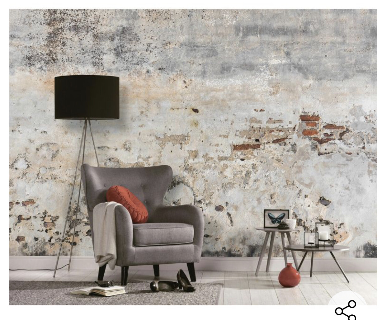 Sitzecke mit grauem Sessel, rotem Kissen, schwarzer Bodenlampe und Beistelltisch vor bröckelnder Wand.