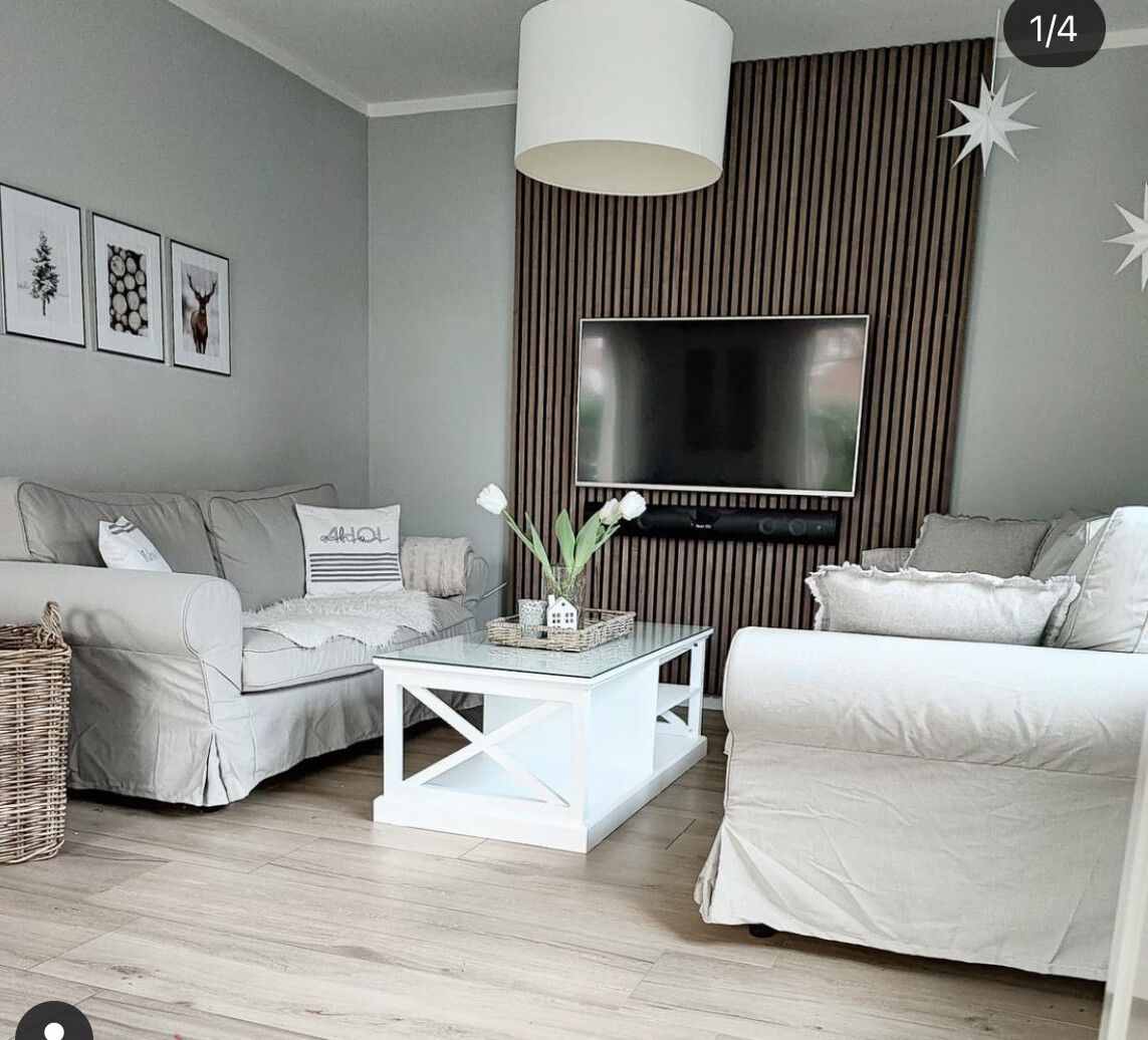 Wohnzimmer mit grauen Sofas, weißem Couchtisch, TV vor Holzpaneel-Wand, Vase mit Tulpen.