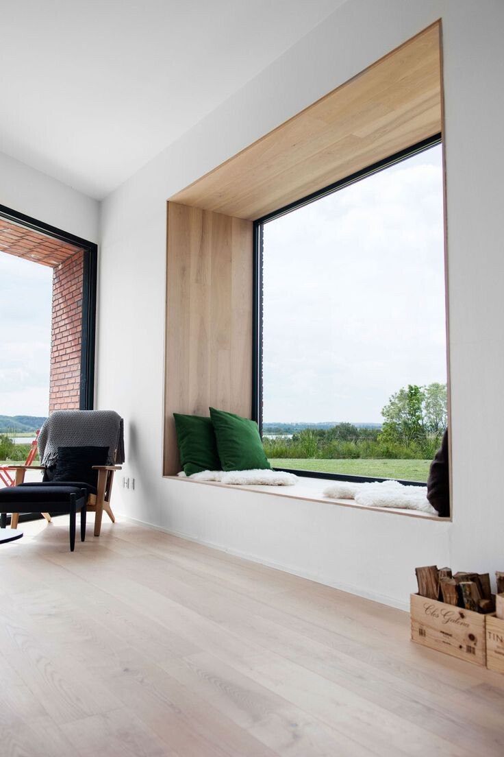 Modernes Wohnzimmer mit Fensterbank-Nische, grünen Kissen und Blick ins Grüne.