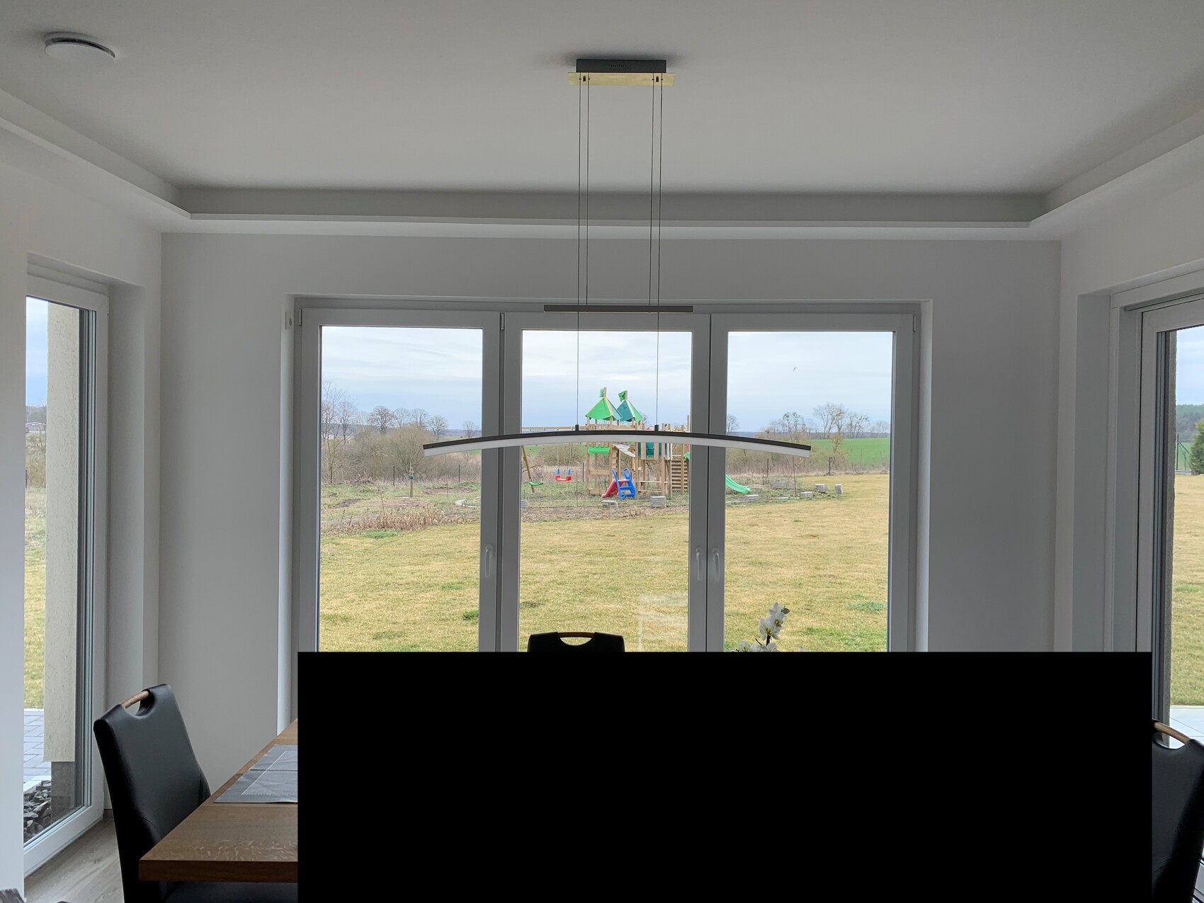 Heller Wohnraum mit Esstisch, schwarzen Stühlen und großer Fensterfront mit Gartenblick.