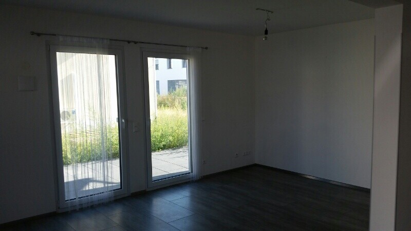 Leeres modernes Wohnzimmer mit großen Glas-Schiebetüren zum Außenbereich und dunklem Boden.