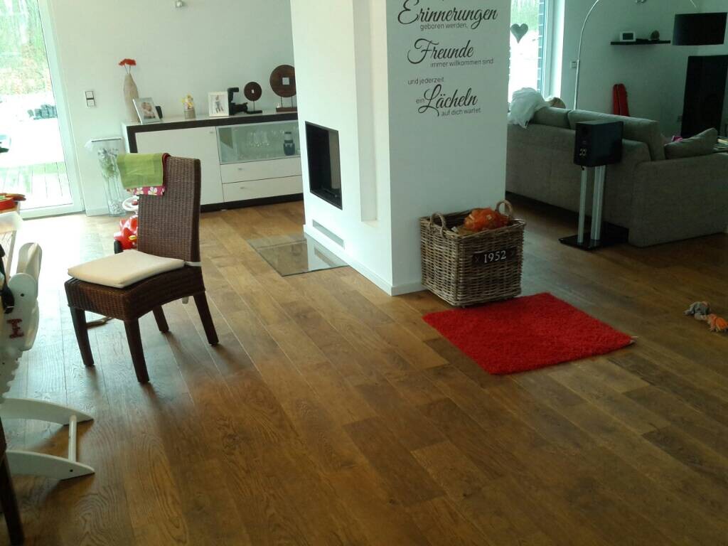 Offenes Wohnzimmer mit Holzboden, brauner Korbsessel, rote Matte und weiße Trennwand.