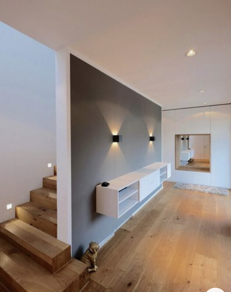 Moderner Wohnraum mit grauer Akzentwand, weißer Konsole, Spiegel und kleinem Hund an der Treppe.