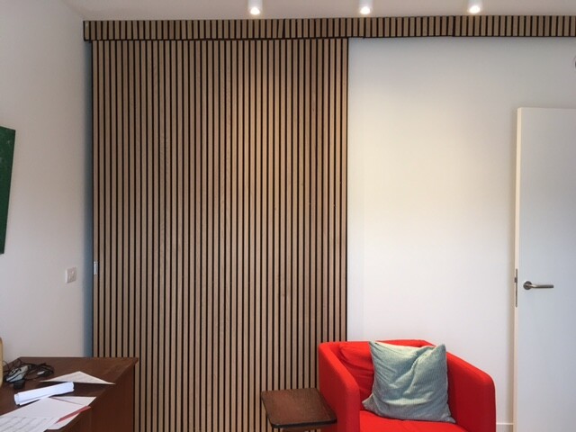 Wohnzimmer-Ecke mit rotem Sessel, vertikaler Holzlatten-Wand und Tür rechts.