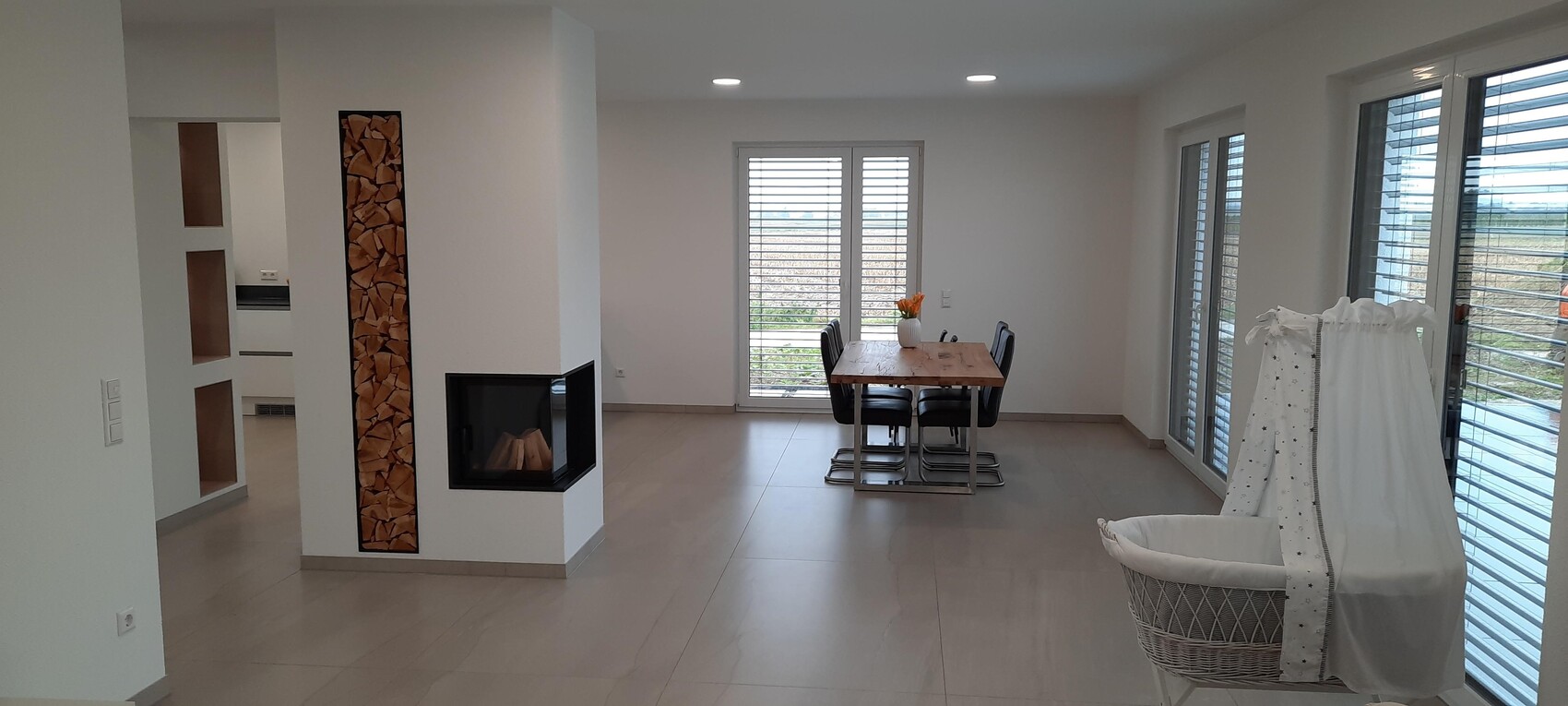 Helles offenes Ess- und Wohnzimmer mit Holztisch, Kamin und großen Fenstern.