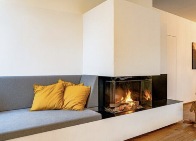 Modernes Wohnzimmer mit Kamin, graues Ecksofa und gelbe Kissen, weiße Wände, Holzboden.