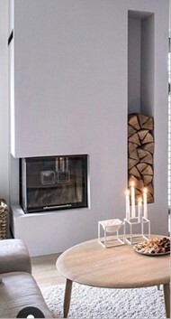 Modernes Wohnzimmer mit Kamin, rundem Holztisch, Kerzen und Holzstapeln neben dem Sofa.