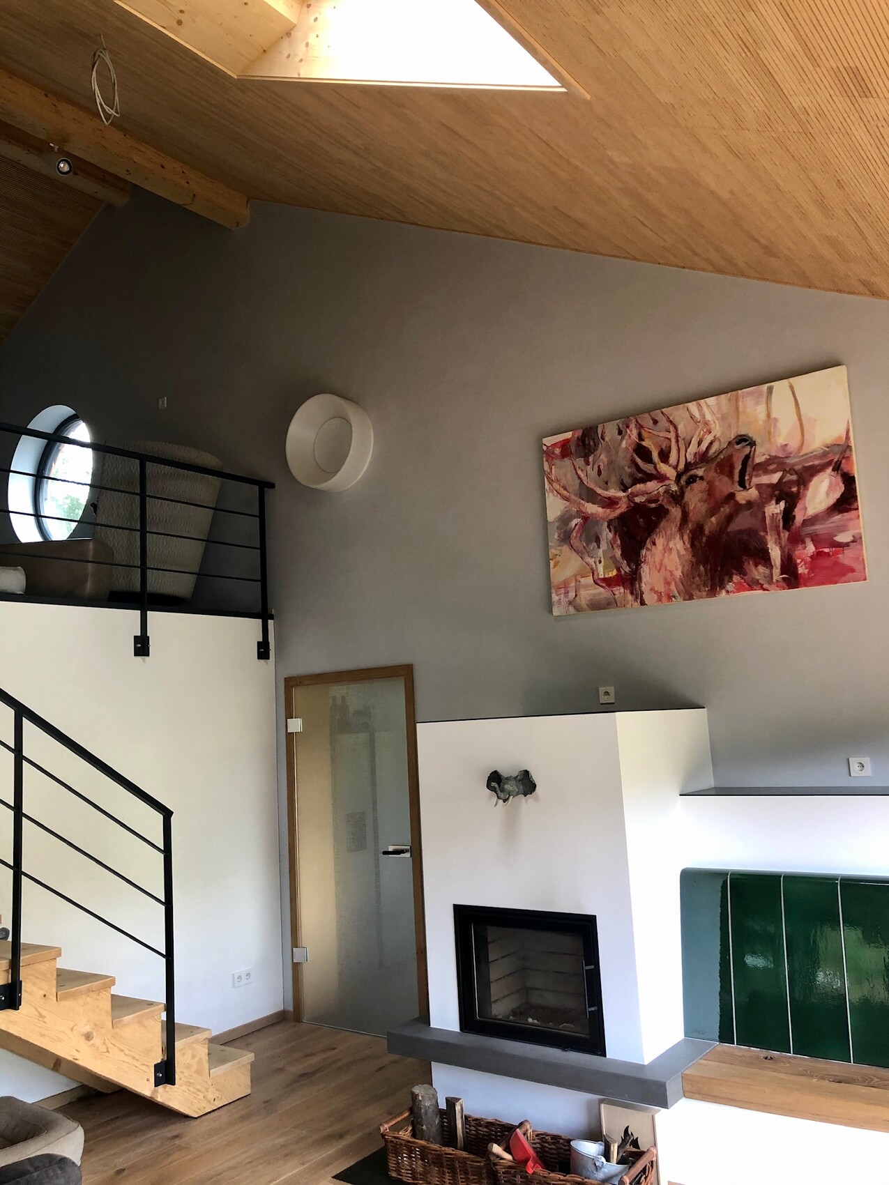 Modernes Loft-Wohnzimmer mit Galerie, Holztreppe, Kamin und abstraktem Hirschbild.