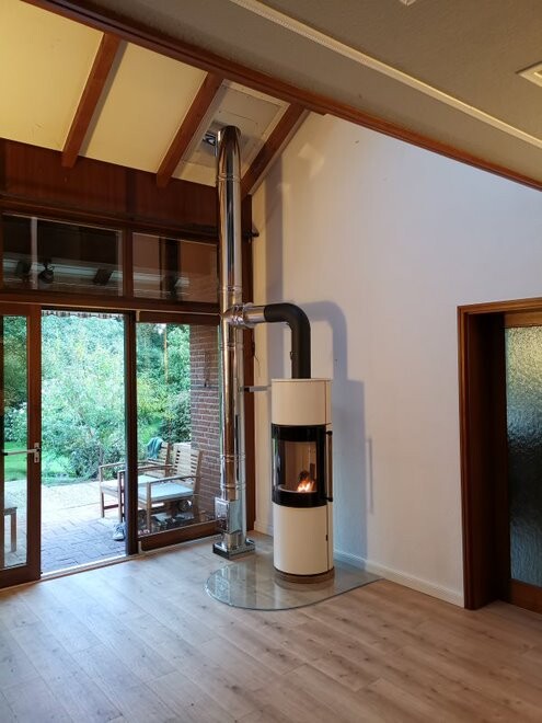 Moderne weiße Kaminofen mit Glassfront und brennendem Feuer, Edelstahl-Abzug, Terrassentür zum Garten.