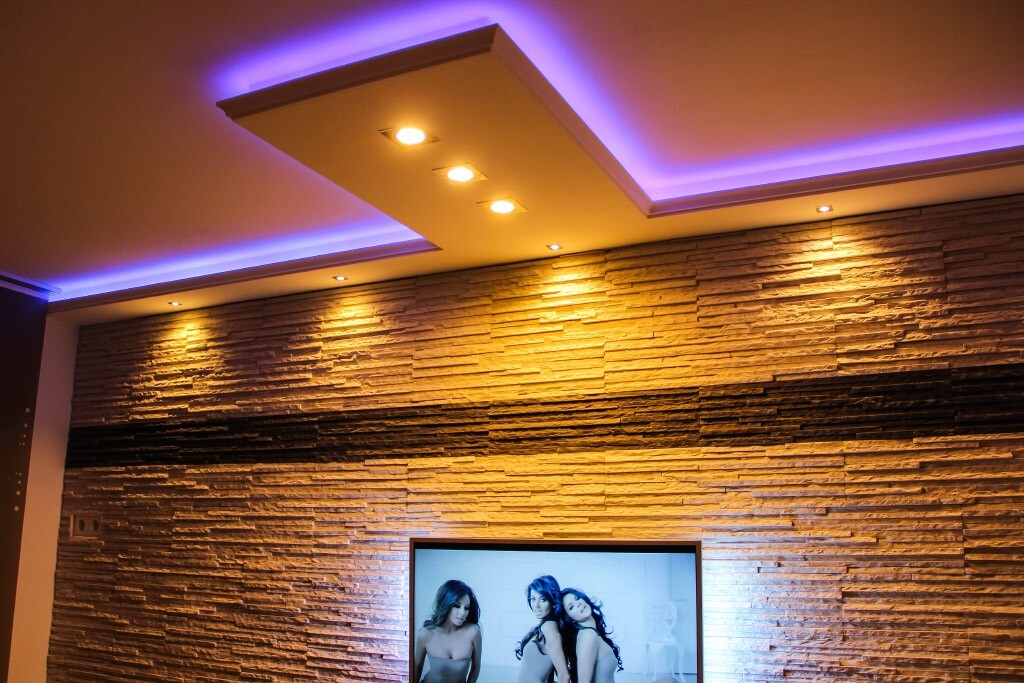 Moderne Steinwand mit violetter LED-Beleuchtung; Fernseher zeigt drei Frauen.