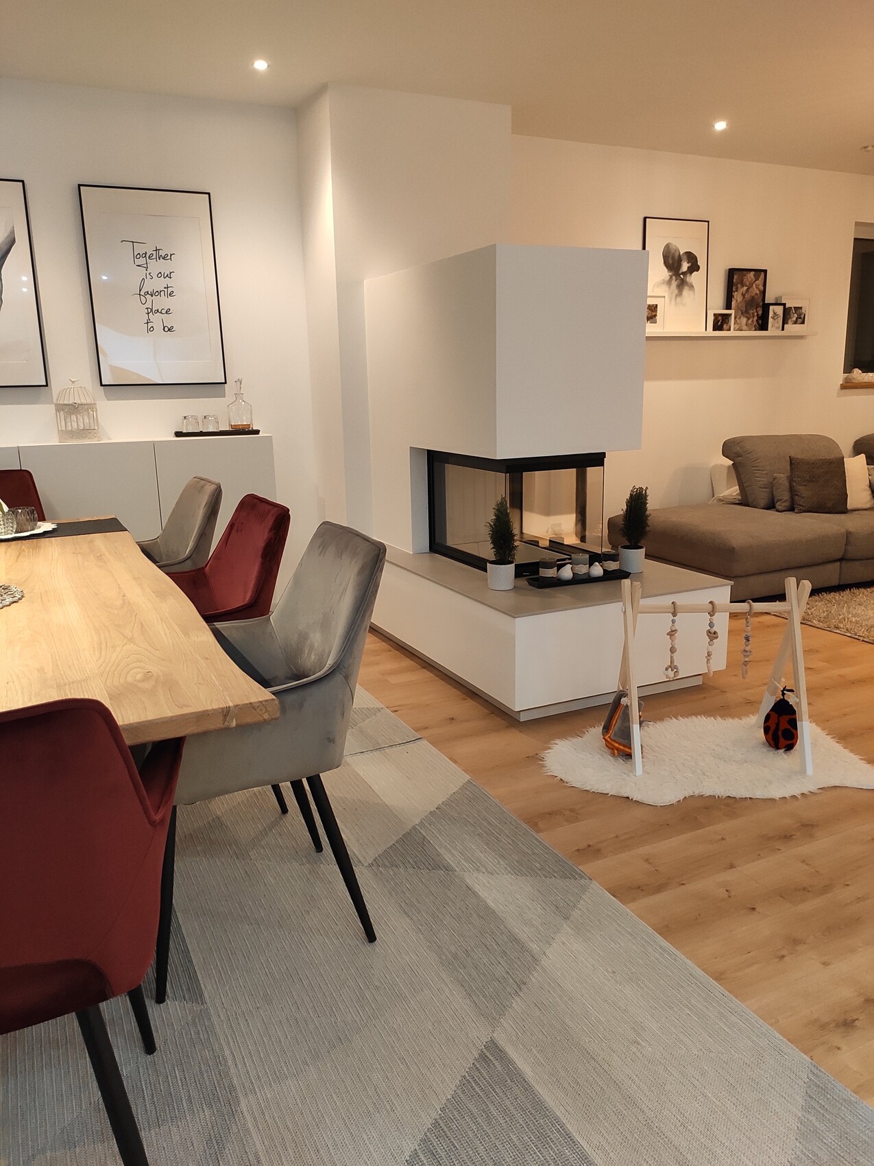 Helles Wohnzimmer mit Kamin, Holztisch, bunt gepolsterte Stühle und Spielbogen auf Teppich