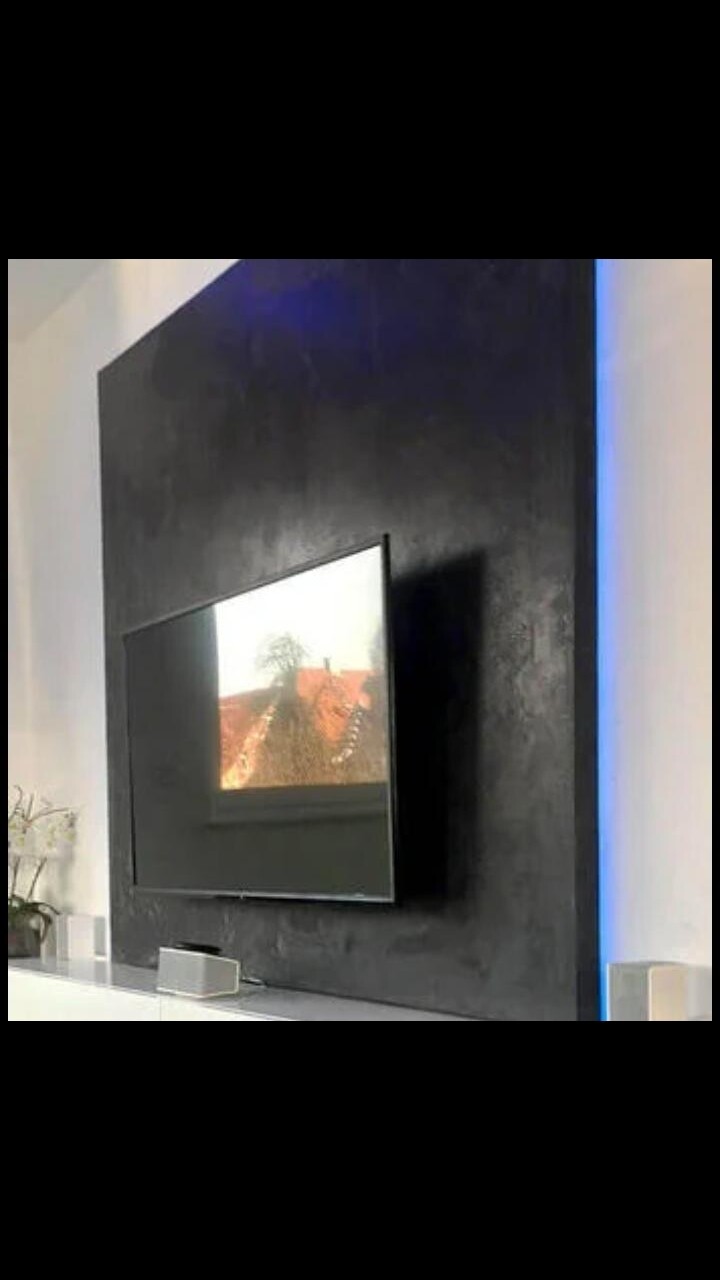 Moderner Wohnraum: Schwarze Wand mit Flachbildfernseher, linke Pflanze, rechts blauer LED-Streifen.