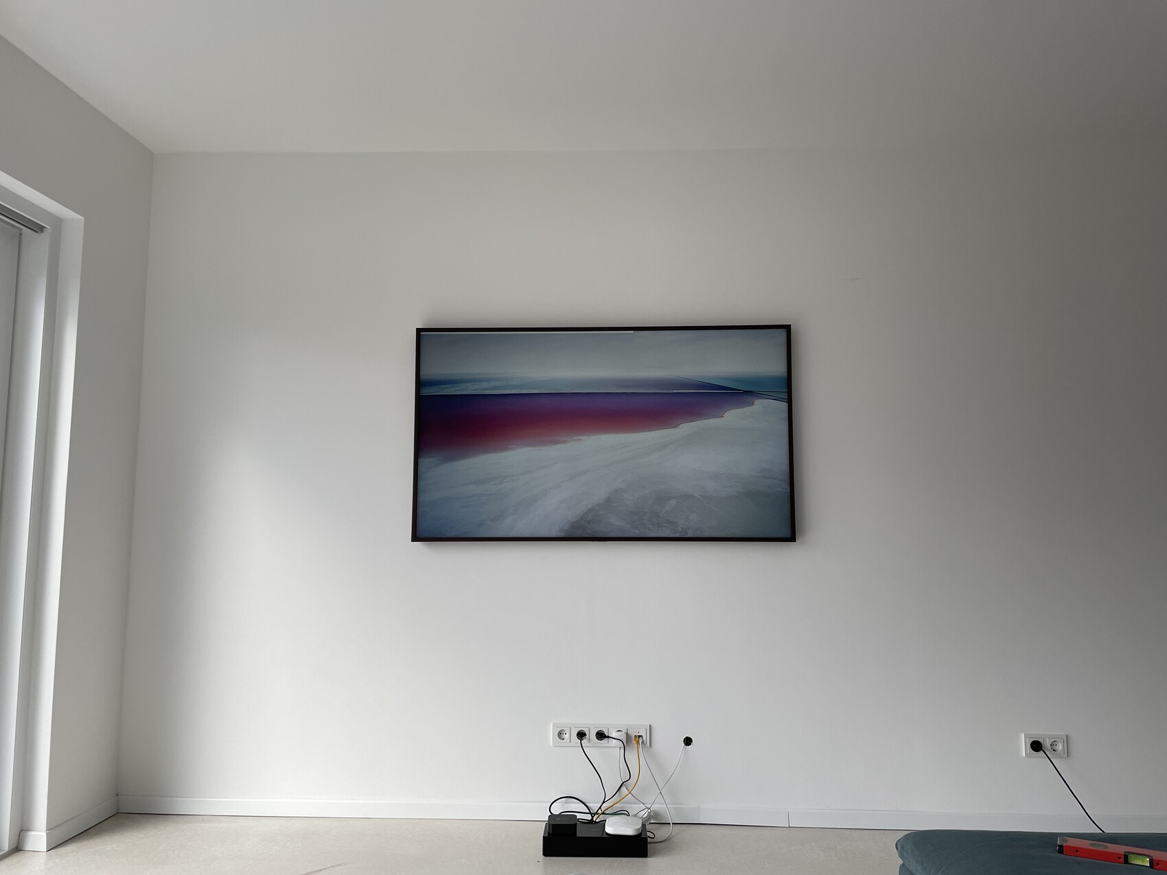 Weiße Wand mit schwarzem Rahmen, Küstenbild; Kabel, Router am Boden, Fenster links.