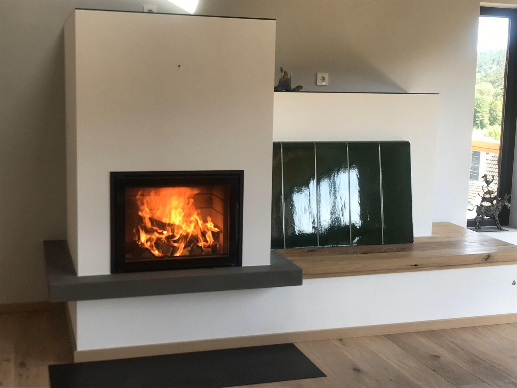 Moderner Wohnraum: Kamin links mit Feuer, daneben grüne Fliesen und Fenster rechts.