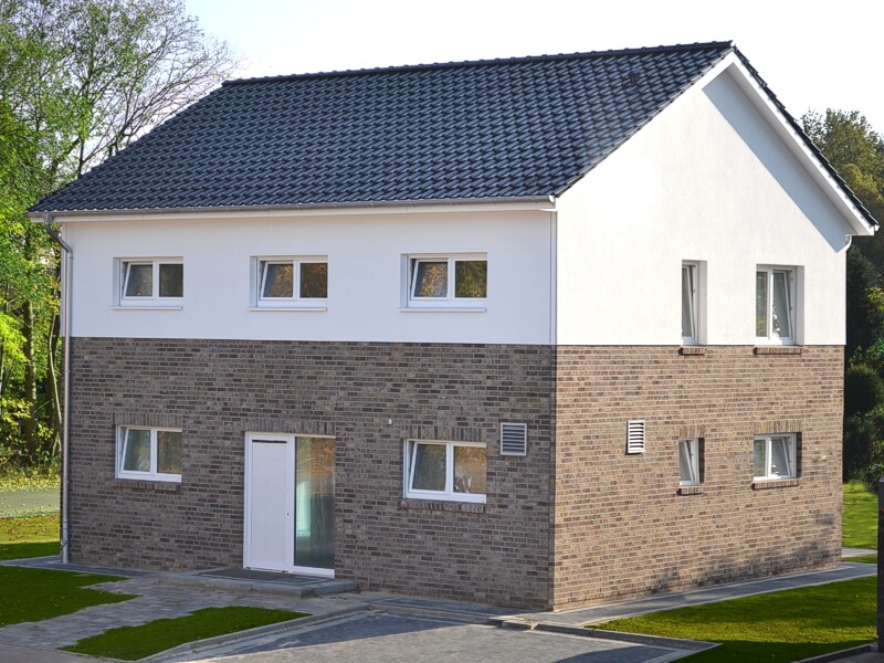 Zweistöckiges Haus mit braunem Klinkerunterteil, weißem Obergeschoss, dunklem Ziegeldach und Garten.