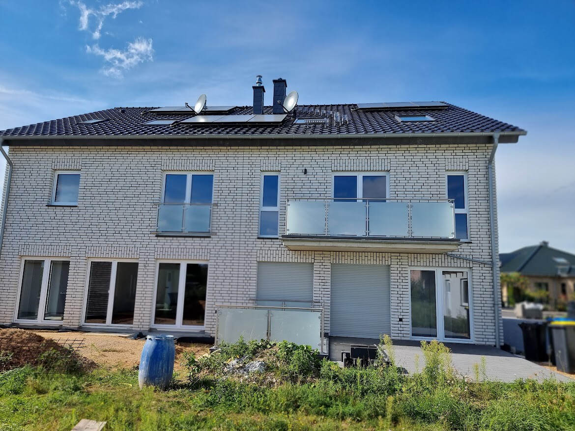 Zweistöckiges weißes Ziegelhaus mit Balkon, Dach-Solaranlage und Satellitenschüsseln