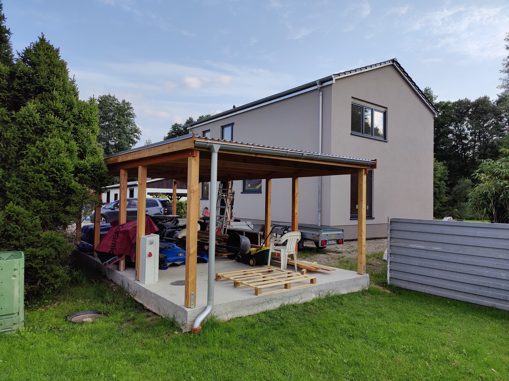 Modernes zweistöckiges Haus mit Holzcarport im Garten, Bauwerkzeuge sichtbar